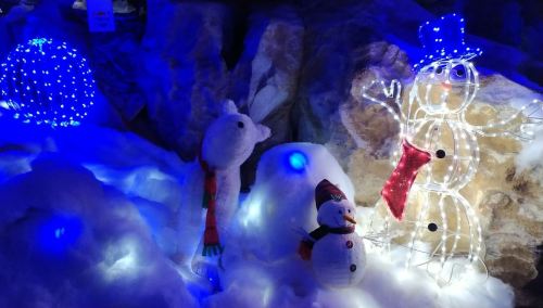A snowy scene with a lit snowman, a snowman figure, and colorful lights in a winter setting.