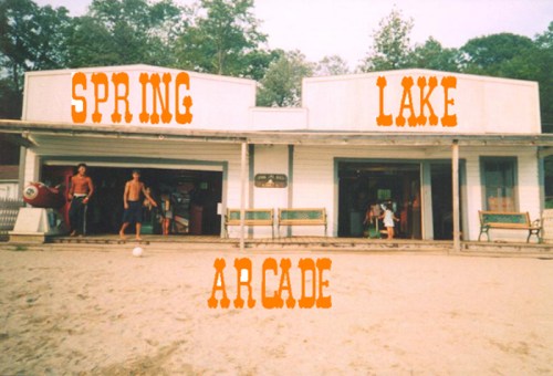 A beachside arcade building with "SPRING LAKE ARCADE" signage, featuring people outside on a sandy area.