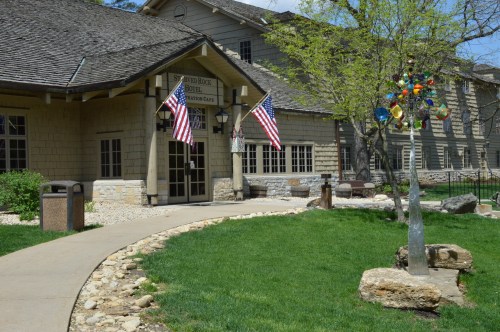 Entrance of Silver Rock Hotel with American flags, a landscaped path, and colorful outdoor art in a sunny setting.