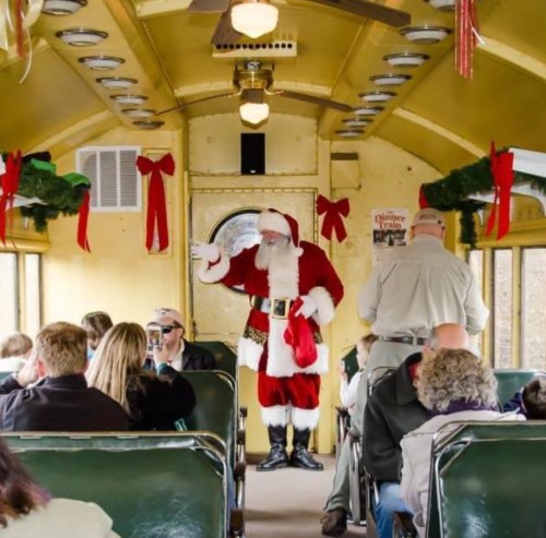 A festive train interior with Santa greeting passengers, decorated with holiday wreaths and ribbons.