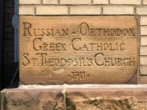 Stone plaque reading "Russian Orthodox Greek Catholic St. Theodosies Church - 1911" on a brick wall.