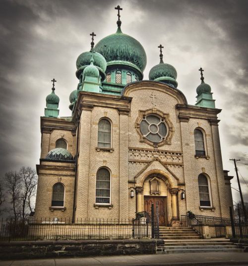 Historic church with green domes and crosses, featuring intricate architecture against a cloudy sky.