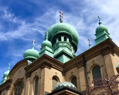 A historic church with green domes and crosses against a blue sky with clouds.