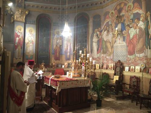A priest conducts a service in a beautifully decorated church with colorful murals and ornate altar.