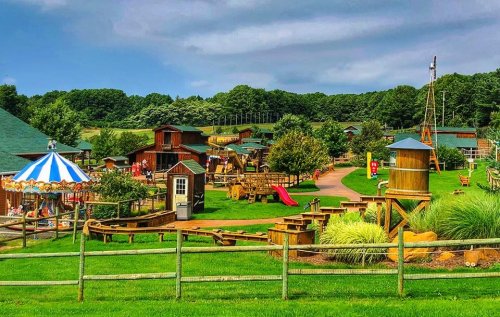 A colorful playground with wooden structures, a carousel, and green lawns under a cloudy sky.