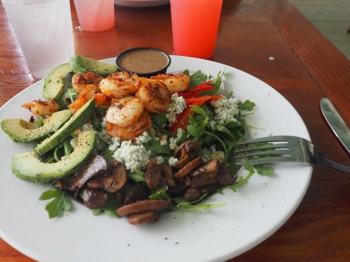 A vibrant salad with shrimp, avocado, red peppers, mushrooms, and blue cheese, served with a dressing on the side.