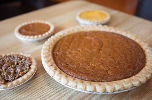 A large pumpkin pie and three smaller pies on a wooden table, showcasing a variety of pie fillings.