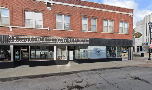 A brick building with storefronts, featuring large windows and a black awning, on a city street.