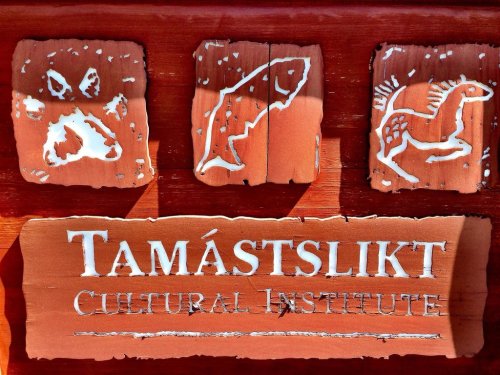 Sign for Tamástslikt Cultural Institute featuring three carved symbols: a paw print, a fish, and a horse.