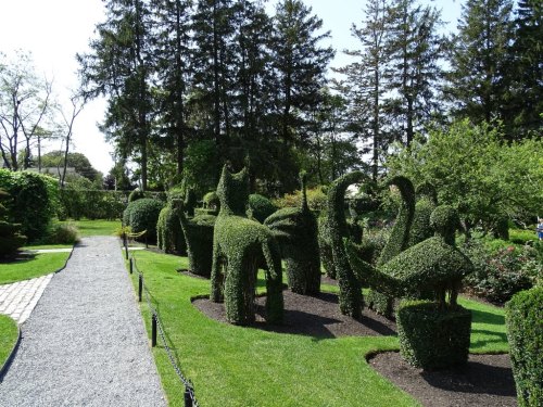 A landscaped garden featuring intricately shaped topiary animals and lush greenery under a clear blue sky.