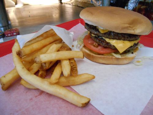 A juicy double cheeseburger with lettuce, tomato, and cheese, served with a side of golden French fries on a red tray.
