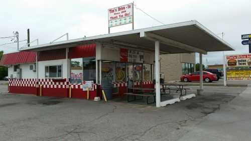 A small drive-in restaurant with a red and white exterior, outdoor seating, and a sign advertising food options.