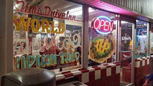 A brightly lit diner window with colorful hand-painted signs reading "Jim's Drive-In," "Open," and various food items.