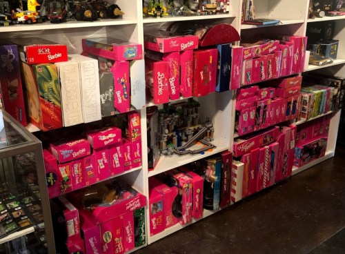 A shelf filled with various pink Barbie doll boxes, showcasing a collection of vintage toys.