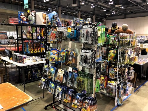 A display of various action figures and collectibles at a convention, with shelves and tables filled with merchandise.