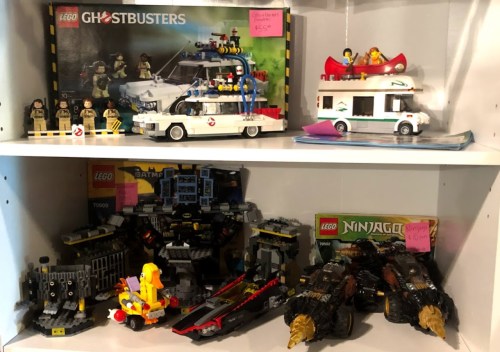 A shelf displaying various LEGO sets, including Ghostbusters, Batman, and Ninjago, with minifigures and vehicles.