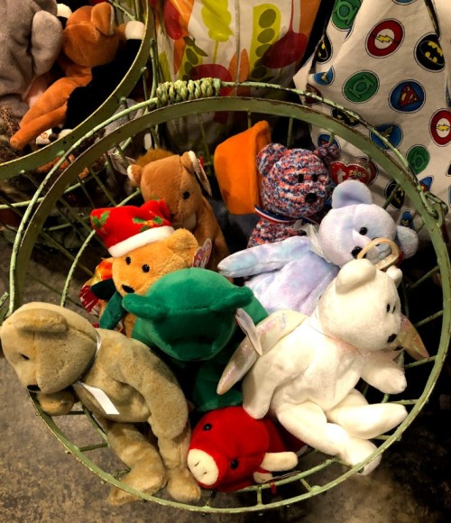 A green wire basket filled with various colorful stuffed animals, including bears and holiday-themed plush toys.