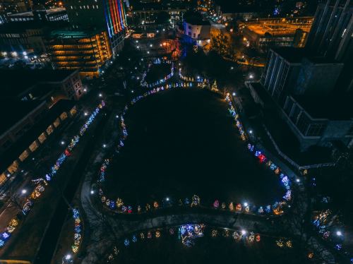 Aerial view of a park at night, adorned with colorful Christmas lights and decorated trees along the pathways.