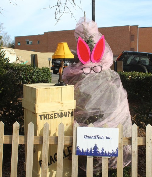 A whimsical display featuring a wrapped figure with bunny ears and glasses, next to a lamp and a sign for QuanlTech, Inc.