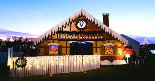 A festive building labeled "Santa's Workshop," adorned with lights and snow, set against a twilight sky.