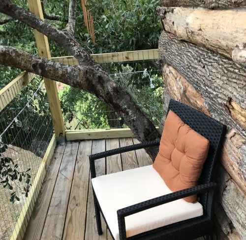A cozy outdoor chair with a cushion, positioned on a wooden deck surrounded by trees and nature.