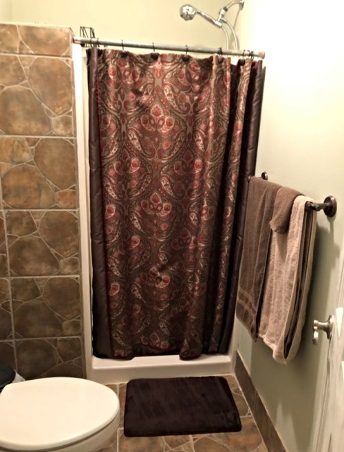 A small bathroom with a shower, patterned curtain, toilet, and towels hanging on the wall.