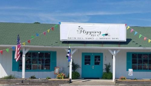 A storefront with a green roof and colorful flags, featuring a sign that reads "Flipping" and windows with blue trim.