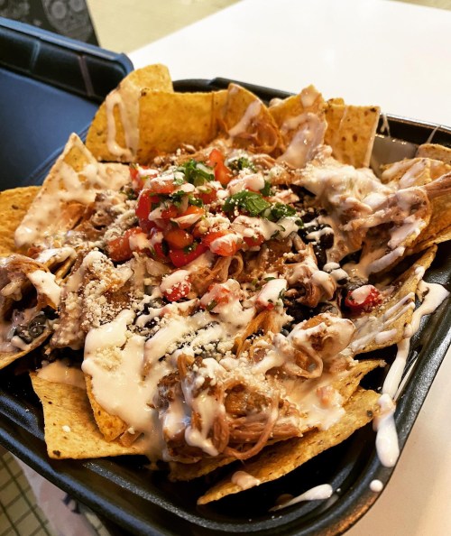 A close-up of nachos topped with pulled pork, pico de gallo, cheese, and drizzled with creamy sauce.