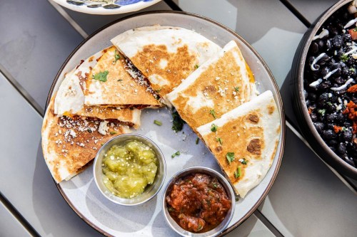 A plate of quesadillas with cheese, garnished with cilantro, served with green and red salsa on the side.