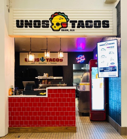 A colorful taco stand named "Unos Tacos" with a vibrant sign and menu display in a casual setting.
