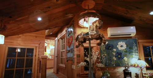Cozy wooden interior featuring a carved horse, floral artwork, and warm lighting in a rustic cabin setting.