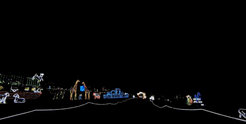 A dark scene featuring colorful holiday lights arranged in various festive shapes and designs along a pathway.