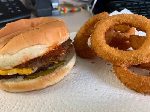 A hamburger with cheese, pickles, and sauce next to a serving of crispy onion rings on a paper towel.