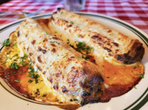 Two golden-brown enchiladas topped with sauce and garnished with parsley, served on a plate with a checkered tablecloth.