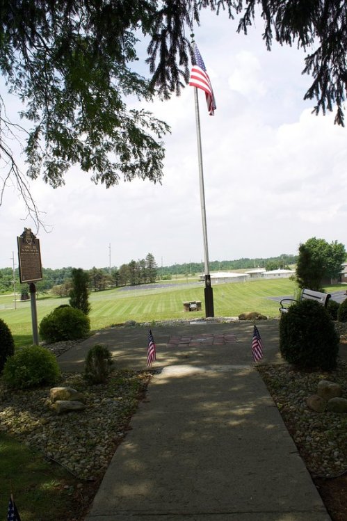 A pathway leads to a flagpole with an American flag, surrounded by greenery and small flags on the ground.