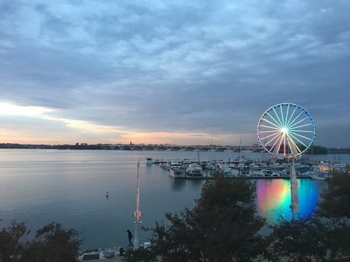 A serene waterfront view at sunset featuring a colorful Ferris wheel and boats docked in the marina.