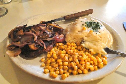 A plate of food featuring a grilled steak with onions, mashed potatoes, and a side of corn.