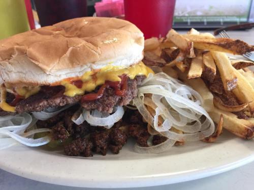 A cheeseburger with ketchup and onions on a plate, accompanied by a side of crispy French fries.