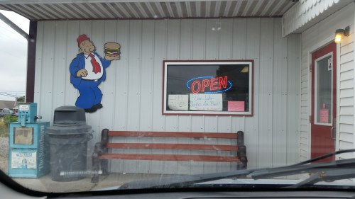 A diner with an "Open" sign, featuring a cartoon chef holding a burger and a bench outside.
