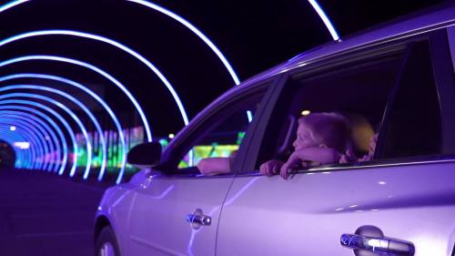 A child leans out of a car window, gazing at colorful lights in a tunnel at night.