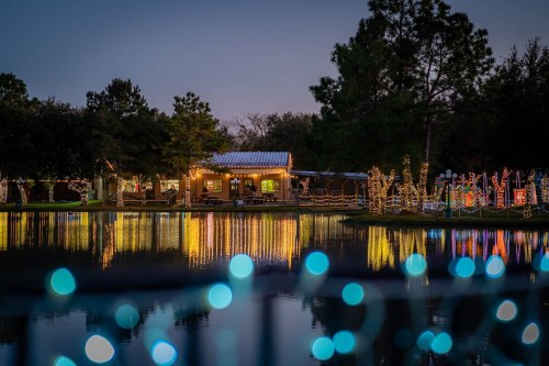 A serene lakeside scene at dusk, featuring a cozy cabin adorned with festive lights reflecting on the water.