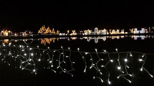 A serene night scene with colorful holiday lights reflecting on water, framed by twinkling white string lights.