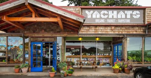 Exterior of Yachats Brewing, Market, and Farmstore with blue doors, wooden accents, and colorful flower planters.