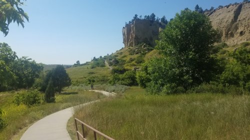 A winding path through lush greenery leads to a rocky cliff under a clear blue sky.