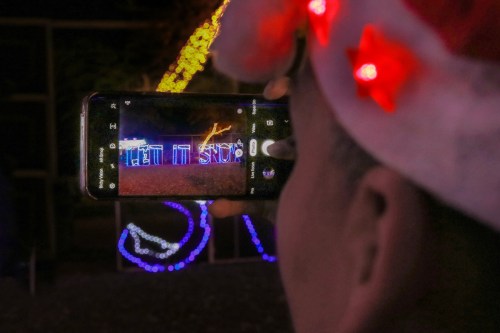 A person in a festive hat takes a photo of colorful Christmas lights with their smartphone.