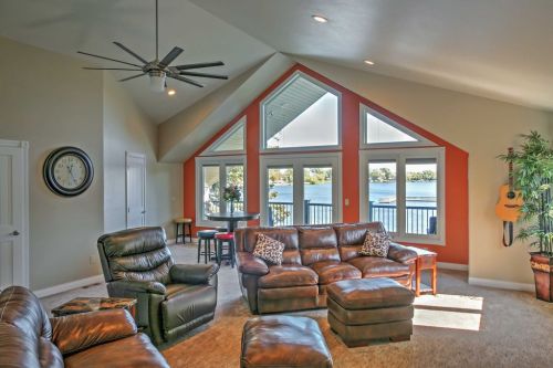 Cozy living room with leather furniture, large windows overlooking a lake, and a ceiling fan. Bright and inviting space.