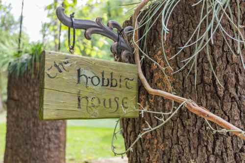 A wooden sign reading "The Hobbit House" hangs from a tree, surrounded by greenery.