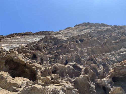A rocky cliff with textured surfaces under a clear blue sky.