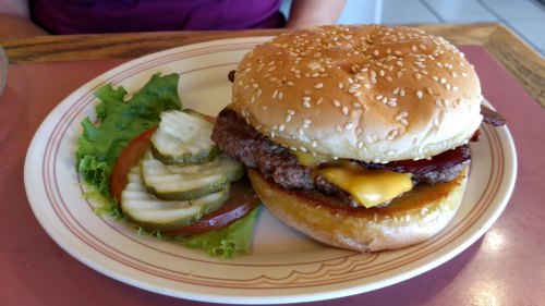 A sesame seed bun burger with cheese, lettuce, tomato, and pickles on a plate.