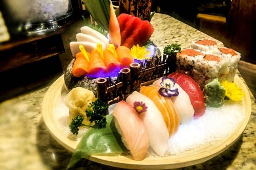 A beautifully arranged sushi platter featuring various types of sushi, sashimi, and garnishes on a wooden tray.